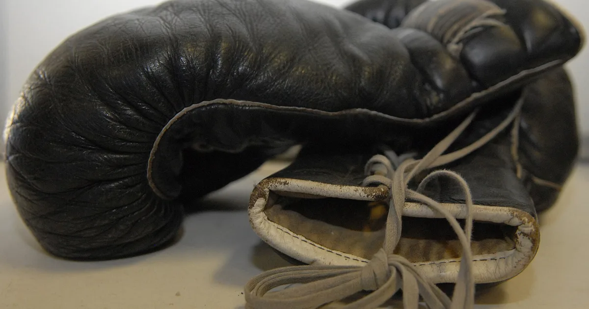 A pair of worn black leather boxing gloves with laces, seen from the side